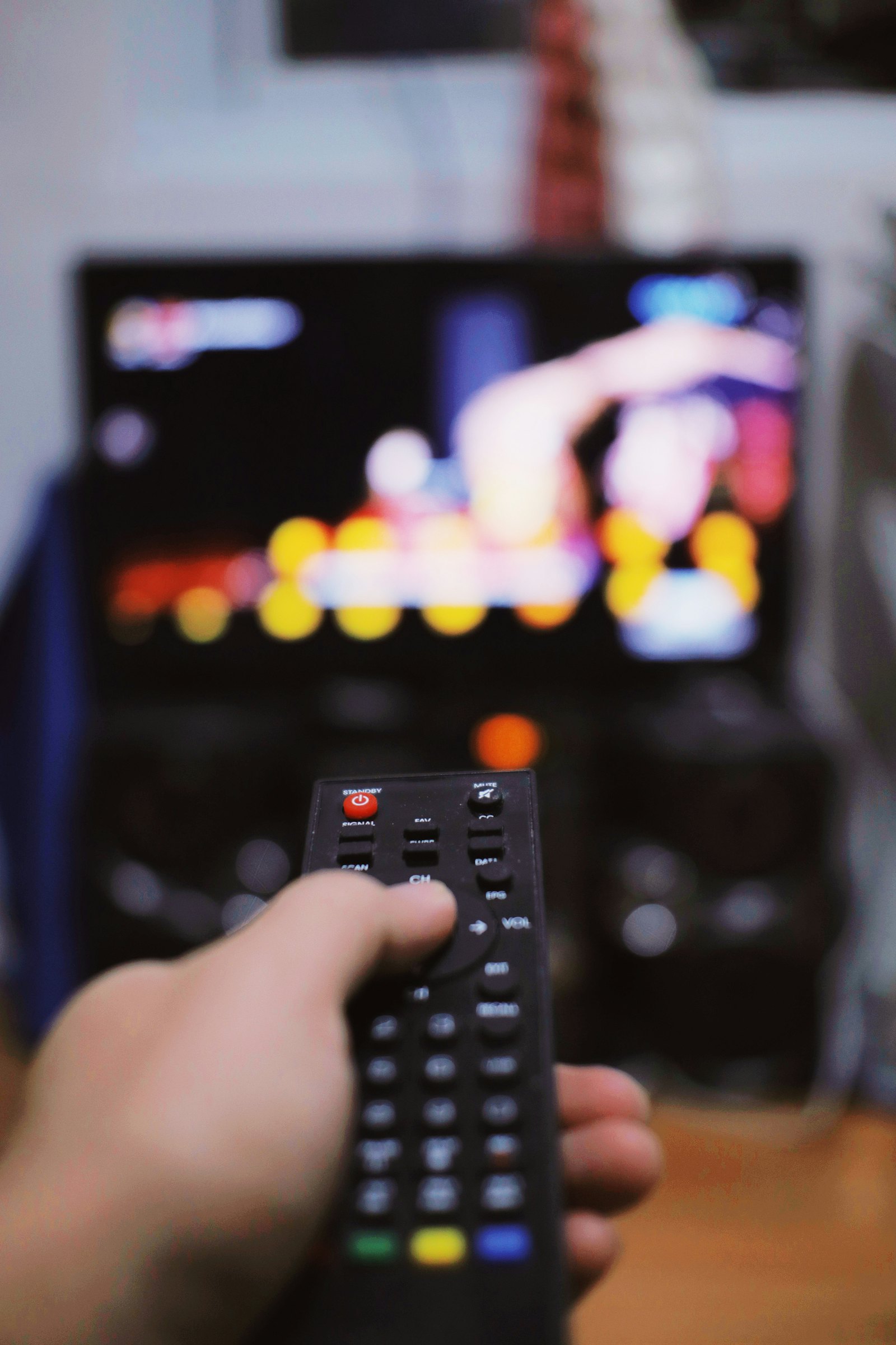 Persoană cu telecomanda în fața televizorului (imagine ilustrativă)